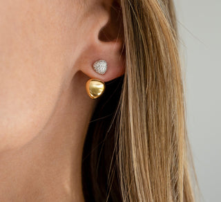 Close-up of a person wearing gold and silver earrings against a neutral background